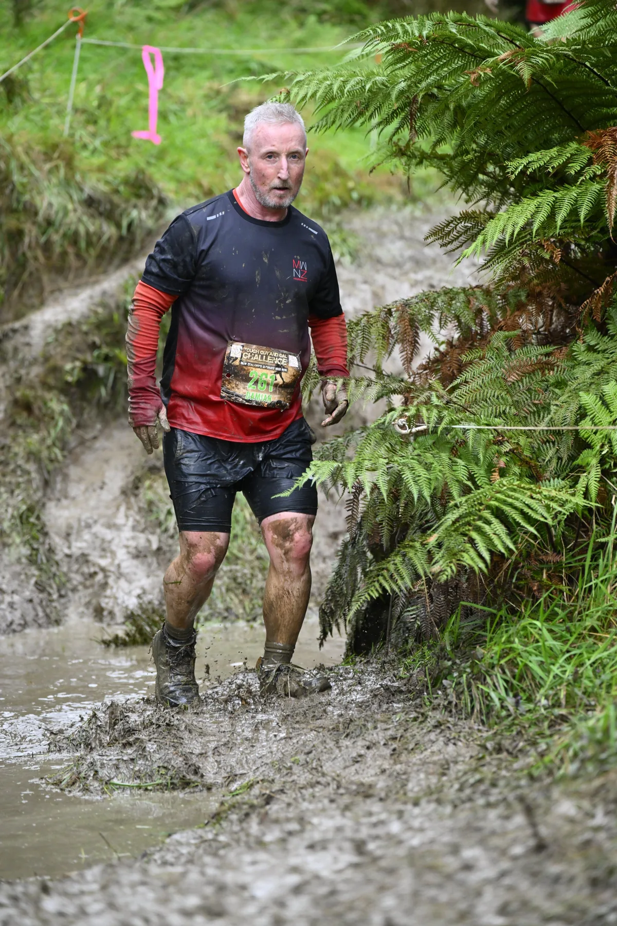 The founder wading through a muddy trench at an obstacle race, covered in mud.