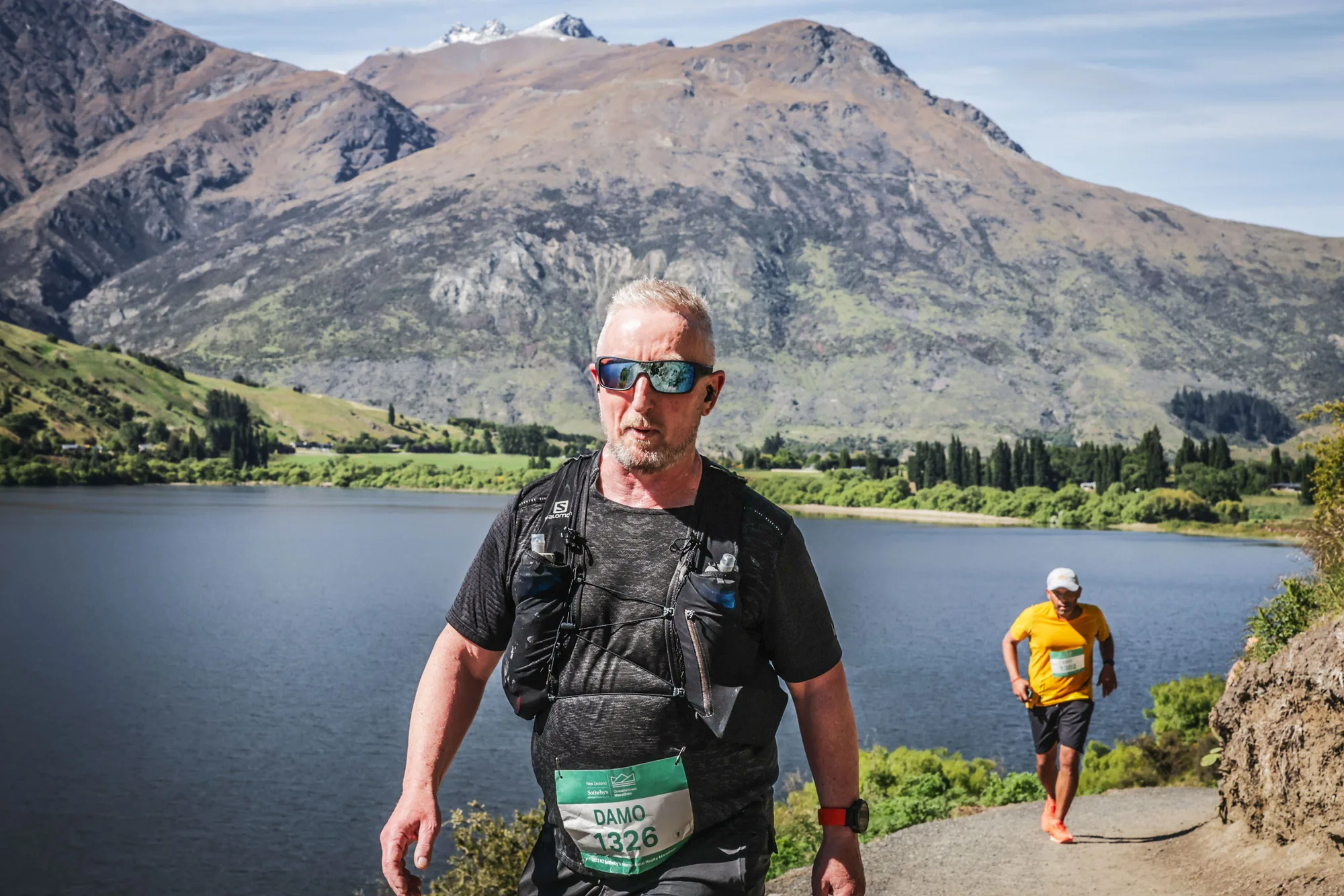 Slow Runners Club's founder on a mountain trail above a lake during a long trail event, wearing a hydration vest.